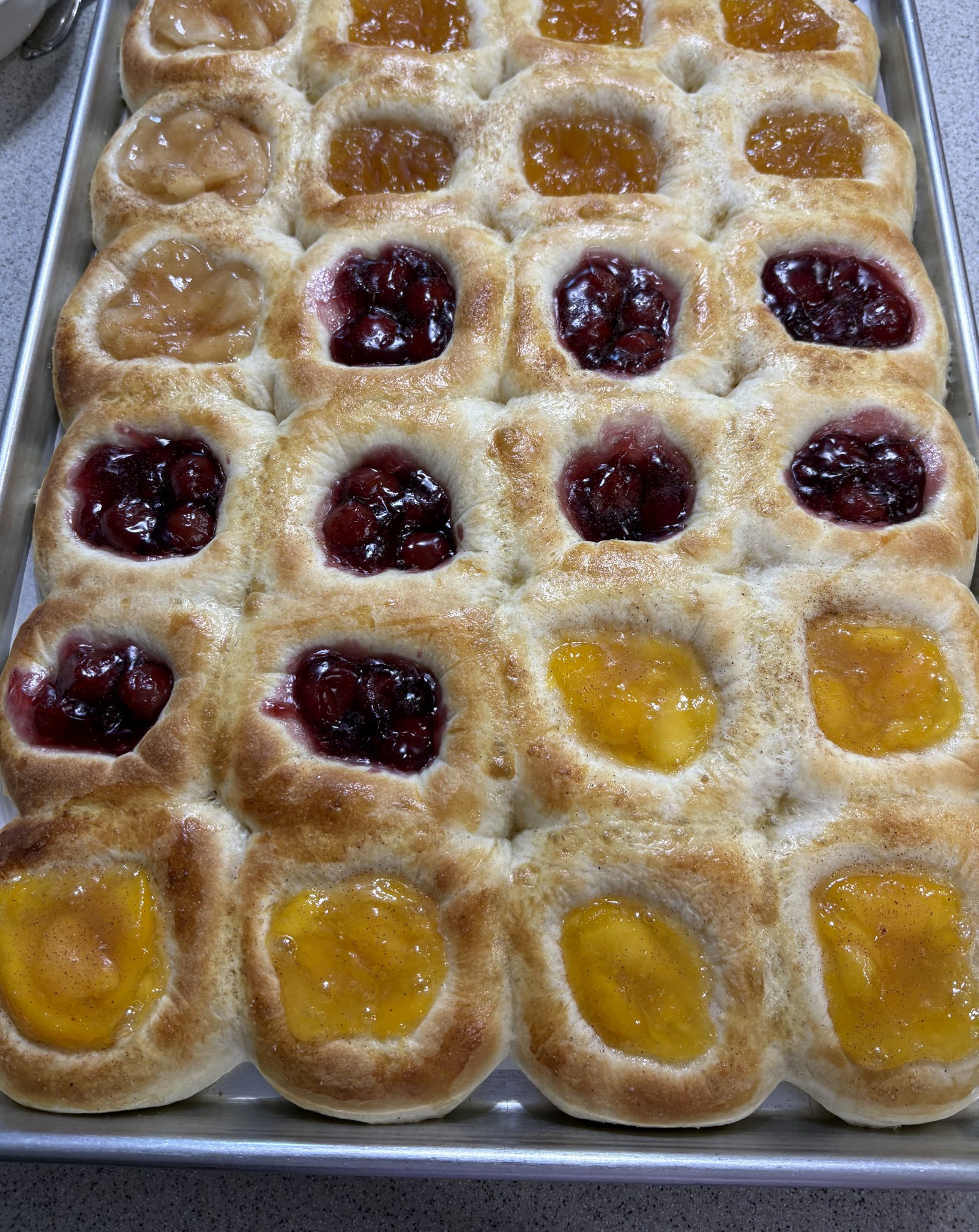 A sheet pan of two dozen homemade kolaches with apple, apricot, cherry, and peach fillings